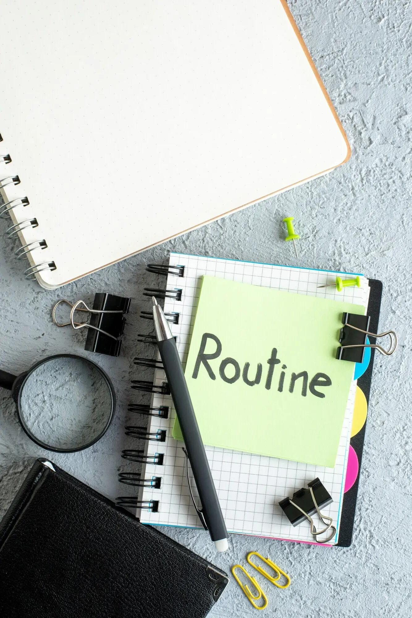 Ansicht von oben: geschriebene Notiz auf grünem Aufkleber mit Notizblock und Stift auf weißem Hintergrund; Routine, Job, Hochschule, Business, Schule, Büro.