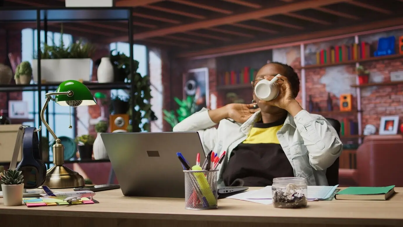 Fröhliche Frau trinkt Kaffee und genießt es, beim Entspannen eine Fernsehsendung anzuschauen.